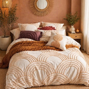May include: A bedroom scene featuring a bed with a cream-colored duvet cover and pillows with a circular design. A rust-colored throw blanket and decorative pillows add texture. A woven mirror and pendant light enhance the warm, inviting aesthetic.