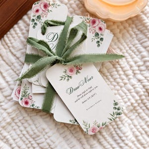 May include: A stack of rectangular paper tags tied with a sage green frayed ribbon. Each tag features a floral design with pink roses and green leaves. The top tag displays the text Draw Near, Draw nigh to God, and he will draw nigh to you. James 4:8 (KJV) Evermere Studio.
