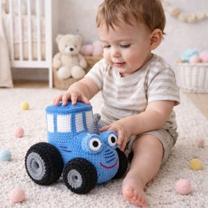 May include: A blue and white crocheted toy truck with black wheels and a smiling face. The toy truck has a rectangular cab with white window details. The toy is designed for children.