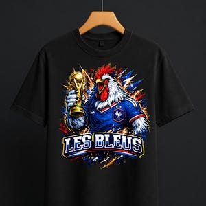 May include: Black t-shirt featuring a rooster in a French soccer jersey holding a gold trophy. The rooster has red, white, and blue accents. The text "LES BLEUS" is displayed in white and yellow.