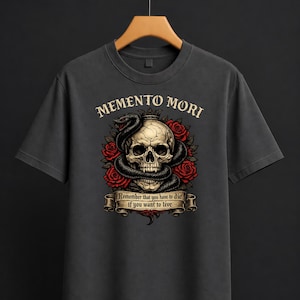 Può includere: T-shirt grigio scuro con un design a teschio, serpente e rose. Il testo "Memento Mori" è sopra il teschio e uno striscione che dice "Remember that you have to die if you want to live."