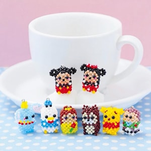 Puede incluir: Una colección de pequeños dijes de cuentas hechos a mano con formas de diversos personajes de dibujos animados. Cada dije está construido con diminutas cuentas de vidrio multicolores, con expresiones faciales y esquemas de color distintos.