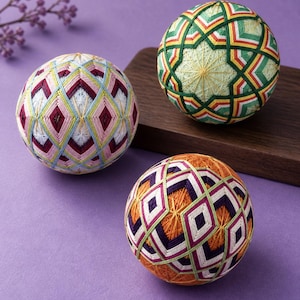 Peut inclure: Trois boules temari sphériques enveloppées de fil à broder complexe et multicolore. Une boule présente des losanges roses, blancs et bleu clair. Une autre affiche des motifs géométriques verts, jaunes et rouges. La troisième a des losanges orange, violets et blancs.