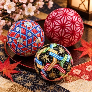 May include: Three spherical temari balls featuring intricate geometric embroidery. One ball displays a red and white pattern, another features blue, red, and white threads, and the third is black with colorful interwoven lines and gold star accents.