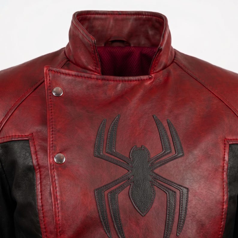 Puede incluir: Chaqueta de cuero roja y negra con un emblema de ara&ntilde;a negra en el pecho. La chaqueta tiene cuello alto, dos cierres de bot&oacute;n a presi&oacute;n plateados y un panel negro en el lado izquierdo. El forro interior es de color rojo oscuro.