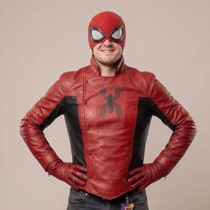 Puede incluir: Chaqueta de cuero roja y negra con un emblema de ara&ntilde;a, usada con guantes a juego y una m&aacute;scara roja con aberturas para los ojos con borde blanco. La chaqueta tiene un dise&ntilde;o de botones asim&eacute;trico.