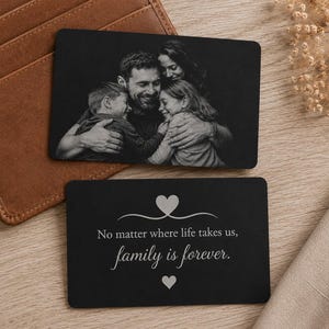 Könnte beinhalten: Zwei schwarze Metallkarten. Eine Karte zeigt ein Familienporträt in Graustufen. Die andere Karte trägt den Text "No matter where life takes us, family is forever" mit zwei Herzsymbolen. Die Karten liegen auf einer Holzoberfläche.