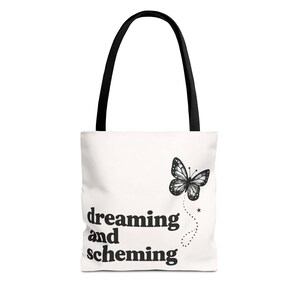 May include: White tote bag with black handles featuring a black and white butterfly illustration and the words "dreaming and scheming" in a bold, black font. The bag is designed for carrying items.