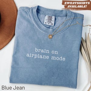 Blue t-shirt with "brain on airplane mode" text and a gold necklace.