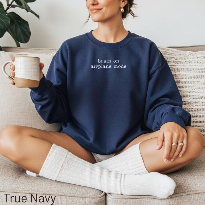 Navy sweatshirt with "brain on airplane mode" text, woman holding mug.