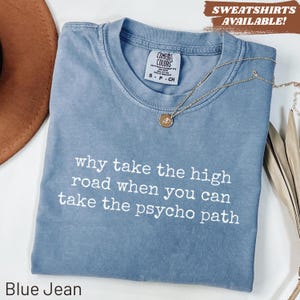 May include: A blue jean colored t-shirt with a crew neckline and a white graphic print that reads, why take the high road when you can take the psycho path. The shirt features a Comfort Colors brand label at the inner neck and a gold necklace.