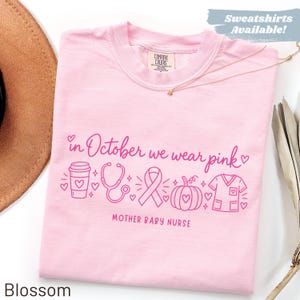 May include: A light pink t-shirt featuring the dark pink text "in October we wear pink" and "MOTHER BABY NURSE". The design includes line art icons of a coffee cup, stethoscope, awareness ribbon, pumpkin, and scrub top with small hearts.