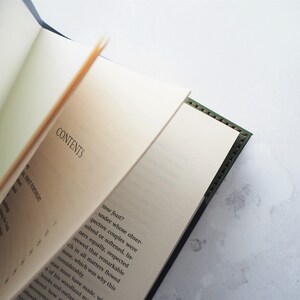 May include: An open book with the word "CONTENTS" visible on the page. The book has a dark green cover with stitched edges. The pages are off-white, and the text is in black. The book is partially open, revealing the text on the pages.