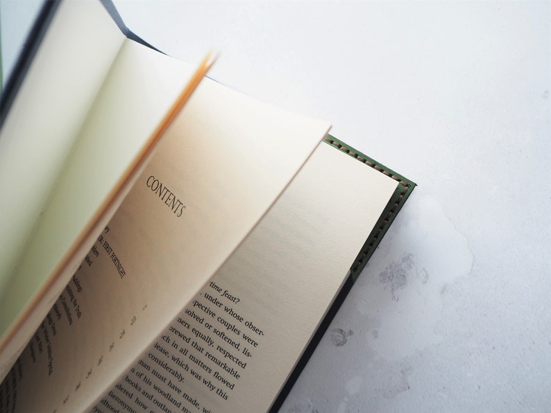 May include: An open book with the word "CONTENTS" visible on the page. The book has a dark green cover with stitched edges. The pages are off-white, and the text is in black. The book is partially open, revealing the text on the pages.