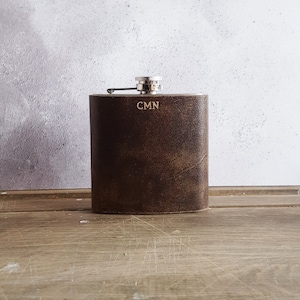 May include: A brown leather-wrapped flask with a silver top and the initials "CMN" engraved on the front.