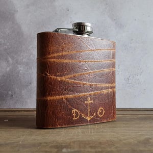 May include: A brown leather-wrapped flask with a silver top and an engraved anchor and initials "D.L.O."
