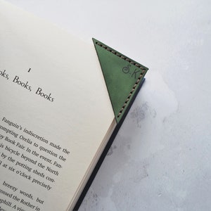May include: Green leather corner bookmark with stitched edges, resting on the pages of a book. The bookmark has the initials "S.K." embossed on it. The book's title is "Books, Books, Books."