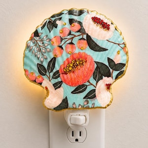May include: A scallop shell night light featuring a light blue background with painted coral and pink flowers, dark green leaves, and small berries. The shell edges are trimmed in gold, and the floral centers are accented with small red and yellow beads.