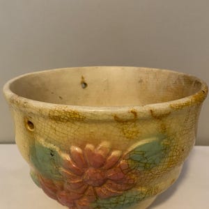 May include: A vintage ceramic hanging planter with a crackled glaze finish. The planter features a floral design with pink and green flowers.
