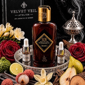 May include: A brown glass bottle of Brown Sugar Babe nourishing body oil with a gold cap, accompanied by two small sample vials labeled 5 ml and 2 ml. The set includes a black box labeled Velvet Veil Atelier, fresh lychees, a lime, a pear, a vanilla flower, and red roses.