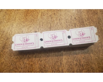 May include: A stack of white paper arcade tickets with purple ink. Each ticket features the Chuck E. Cheese's logo, a cartoon mouse head, and the text: Redeemable only at Participating Locations, No Cash Value, and a serial number.