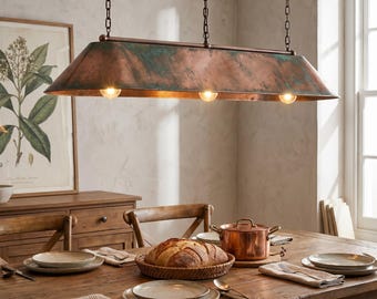 Puede incluir: Una lámpara colgante rectangular con acabado de cobre desgastado y detalles de pátina verde. La pantalla metálica alargada está suspendida por tres cadenas y alberga tres bombillas brillantes que proyectan luz cálida hacia abajo.