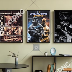 Puede incluir: Tres carteles enmarcados del juego Counter-Strike. Los carteles presentan escenas de acción con soldados y armas. La paleta de colores incluye tonos de marrón, azul y negro. Los carteles se exhiben en una pared verde claro.