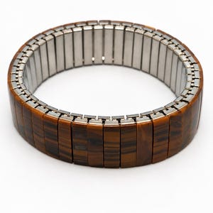 Könnte beinhalten: Ein elastisches Armband mit rechteckigen Tigeraugen-Steinsegmenten, die in einer durchgehenden Schlaufe angeordnet sind. Die Außenseite zeigt braune und schwarze Streifenmuster, während die Innenseite einen silberfarbenen Metall-Dehnmechanismus offenbart.