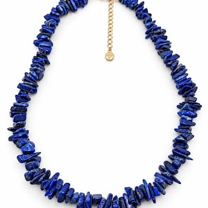 Peut inclure: Un collier composé de nombreuses pépites de lapis-lazuli bleu profond, irrégulières et polies. Les pierres sont enfilées et comportent un fermoir mousqueton en métal doré, une courte chaînette de réglage et une petite breloque ronde dorée.