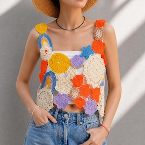 Könnte beinhalten: Ein farbenfrohes Häkeltop mit verschiedenen floralen und abstrakten Formen in Gelb, Orange, Blau, Lila und Creme. Das Top wird über einem weißen Kleidungsstück getragen und mit blauen Jeans kombiniert. Das Häkeldesign ist der Fokus.