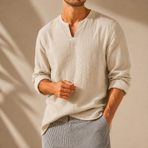 May include: A long-sleeved beige shirt with a split V-neckline and a textured fabric finish, paired with trousers featuring a vertical white and dark blue pinstripe pattern. The shirt has a relaxed fit with slightly rolled-up sleeves at the cuffs.