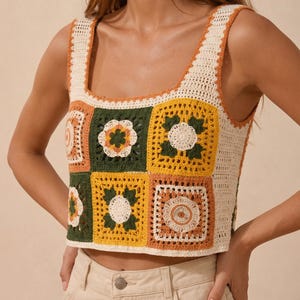May include: A square-neck crochet top with a patchwork design. The top features a cream-colored base with squares in shades of green, yellow, orange, and cream, each with a floral motif. The straps and neckline are trimmed in orange.