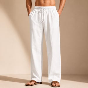 May include: White loose-fitting trousers featuring an elasticated waistband with a drawstring closure. The trousers have a straight-leg cut and are constructed from a textured fabric, reaching down to the ankles, worn with brown slide sandals.
