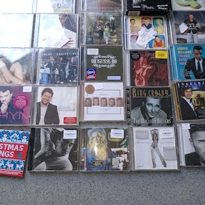 Puede incluir: Una colección de CDs de música variados, con artistas como Sinatra, Keane y Christina Aguilera. Los CDs están en sus estuches originales, mostrando las portadas y títulos de los álbumes. La colección incluye un CD navideño.