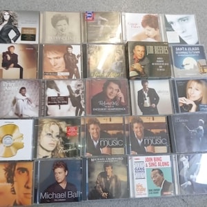 May include: A collection of music CDs featuring various artists. The album covers display images of musicians and album titles. The CDs are in clear plastic cases, and the collection includes artists like Patsy Cline and Engelbert Humperdinck.