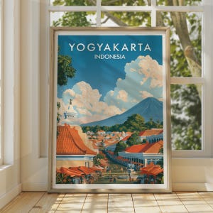 Könnte beinhalten: Ein gerahmtes Reiseplakat mit einer Landschaftsillustration von Yogyakarta, Indonesien. Das Bild zeigt eine Stadt mit orangefarbenen Dächern, einem weißen Tempelbau, grünen Bäumen und einem großen Berg unter einem blauen Himmel mit Wolken.