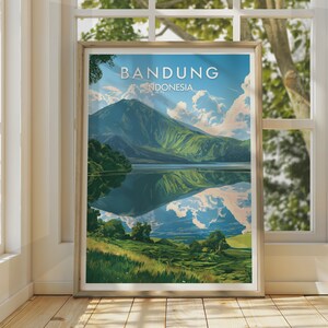 Può includere: Un poster da viaggio incorniciato con un'illustrazione paesaggistica di Bandung, Indonesia. L'opera raffigura una grande montagna verde che si riflette in un lago calmo sotto un cielo blu con nuvole bianche, con il testo BANDUNG INDONESIA in alto.