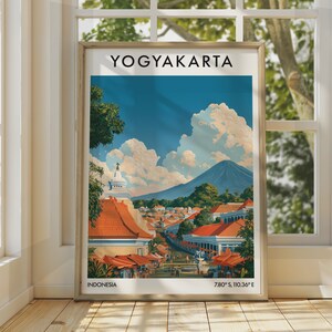 May include: A framed travel poster of Yogyakarta, Indonesia, featuring a landscape illustration with orange-roofed buildings, a white stupa, lush green trees, and a large mountain under a blue sky with white clouds. The text reads YOGYAKARTA and 7.80° S, 110.36° E.