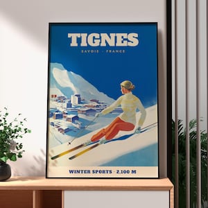 Puede incluir: Un póster de viaje de estilo vintage enmarcado de Tignes, Saboya, Francia. La obra muestra a una persona esquiando con un suéter crema y pantalones naranjas en una ladera nevada, con un pueblo de montaña al fondo. Texto TIGNES SAVOIE FRANCE y WINTER SPORTS 2.100 M.