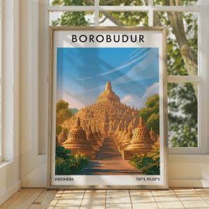 Könnte beinhalten: Ein gerahmtes Reiseplakat mit einer Illustration des Borobudur-Tempels in Indonesien. Der Druck zeigt die steinernen Stupas, eine zentrale Kuppel und eine Treppe unter blauem Himmel. Der Text lautet BOROBUDUR, INDONESIA und 7.61° S, 110.20° E.