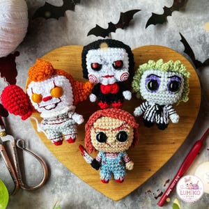 May include: Four small crocheted dolls representing horror characters. One has orange hair and a red balloon, one has black hair and red spiral cheeks, one has green hair and a striped suit, and one has red hair and holds a small white knife.