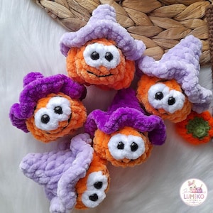 May include: Five crocheted plush pumpkins, each wearing a soft witch hat in shades of light purple or dark purple. The pumpkins are bright orange with large white eye patches and black plastic safety eyes. A small logo reads LUMIKO STORE.
