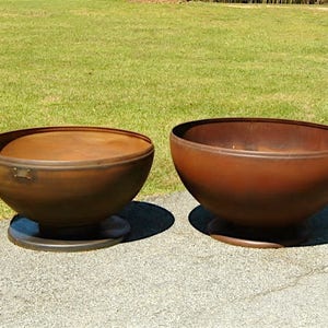 May include: Two large, rusty metal bowls on a concrete surface. The bowls are round and have a slight lip around the top. They are both sitting on a circular base.