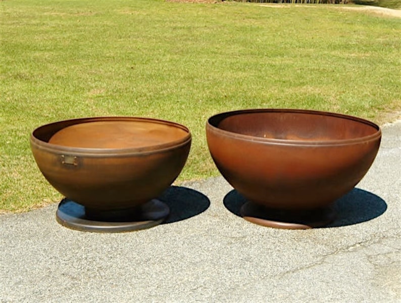 May include: Two large, rusty metal bowls on a concrete surface. The bowls are round and have a slight lip around the top. They are both sitting on a circular base.