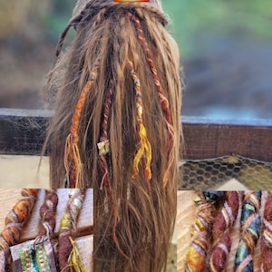 May include: A head of long, light brown hair with multiple colorful dreadlock wraps. The wraps are in shades of orange, yellow, and brown. The image includes a small square logo with the text "aya" and "Soul Spirit Doll".