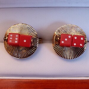 May include: A pair of gold cufflinks with red dice on top. The dice are white with black dots.