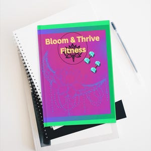 Puede incluir: Un diario de fitness titulado "Bloom & Thrive Fitness" con una cubierta rosa y morada, borde verde y diseño floral azul. La portada también presenta una flor de loto y pesas.
