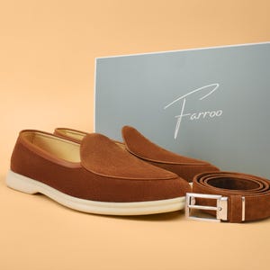 A pair of brown suede loafers with a matching belt and a light blue box with the brand name "Farroo" in white script. The loafers have a white sole.
