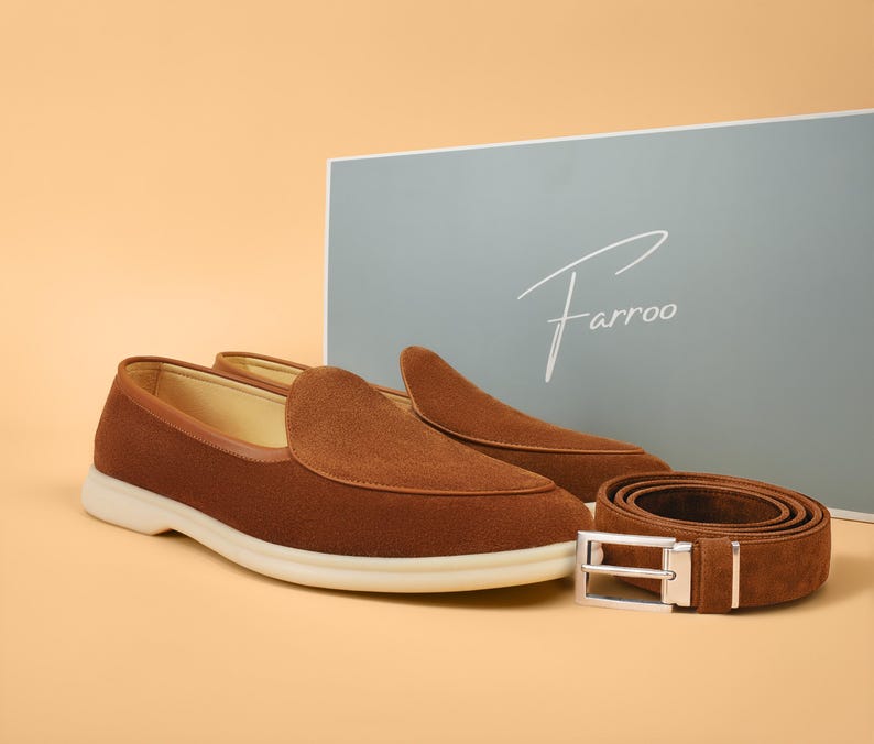 A pair of brown suede loafers with a matching belt and a light blue box with the brand name "Farroo" in white script. The loafers have a white sole.