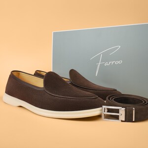 May include: A pair of brown suede loafers with white soles and a matching brown belt with a silver buckle. The items are displayed with a box that has the brand name "Farroo" on it.